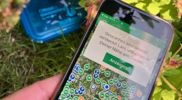 Smartfon pokazuje mapę z zaznaczonymi skrytkami. To jest właśnie geocaching – zabawa w poszukiwanie ukrytych skarbów.