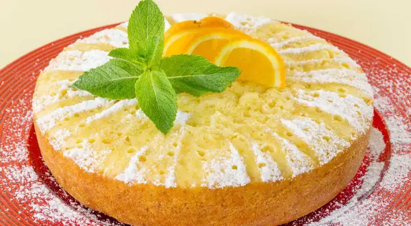 Torta soffice all'arancia, ricetta della nonna, decorata con fettine d'arancia e menta fresca, cosparsa di zucchero a velo.