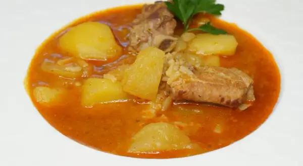 Costillas guisadas con patatas, un plato reconfortante con trozos de carne tierna y patatas en una salsa rojiza, adornado con perejil fresco.