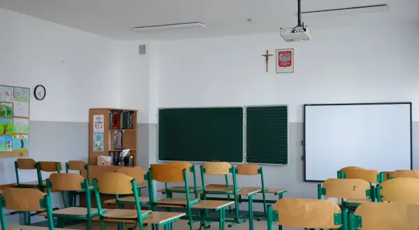 Pusta sala lekcyjna z ławkami, tablicą i projektorem.