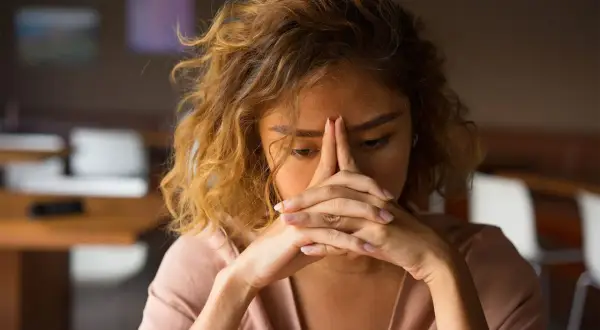 Een vrouw met haar handen voor haar gezicht, die zich terugtrekt uit de wereld. Ze lijkt overgevoelig voor geluid en prikkels, zoekend naar rust.