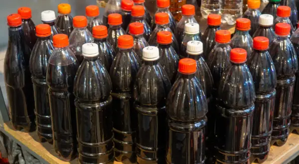 Butelki z ciemnym płynem, być może domowym winem cannonau, stoją obok siebie na półce.