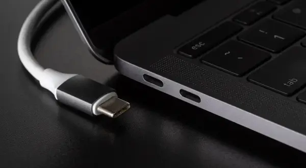 Kabel USB C zbliża się do portu laptopa. Widać jego metalową wtyczkę i biały kabel.