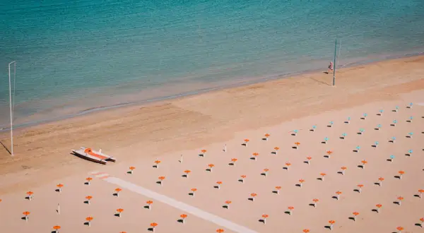 Pusta plaża w Rimini z rzędem parasoli i łodzią ratunkową.