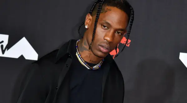 Travis Scott w czarnej koszuli i naszyjnikach na tle logo MTV.
