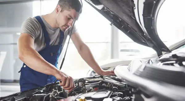 Mechanik w niebieskim kombinezonie pracuje przy silniku. Zastanawiasz się, czy warto płacić za przedłużoną gwarancję w warsztacie sieciowym zamiast u pana Mirka?