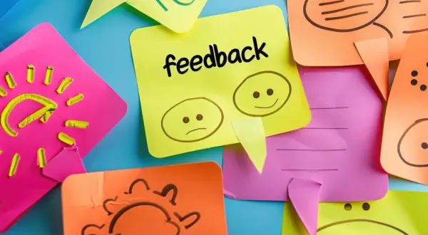 Kolorowe karteczki z rysunkami i napisem "feedback". Jedna pokazuje smutną i wesołą buźkę, symbolizując konstruktywny feedback.