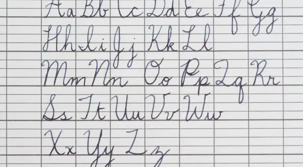 The alphabet in cursive, from A to Z, is written in neat blue ink on lined paper. The handwriting is perfect in cursive, showing each letter's formation.