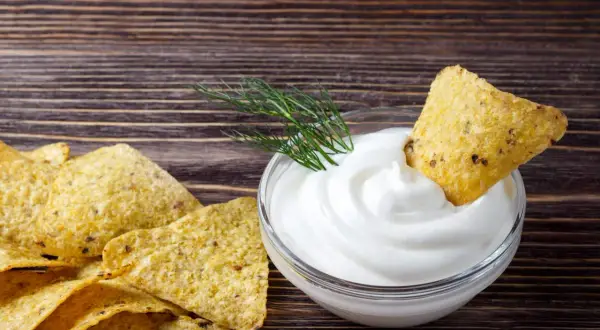 Nachos z gęstym, białym sosem śmietanowym i gałązką koperku na drewnianym tle.