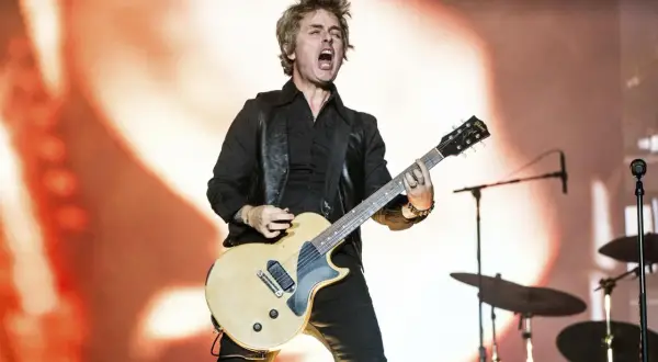 Billie Joe Armstrong z Green Day Saviors śpiewa i gra na gitarze na scenie, z perkusją w tle.