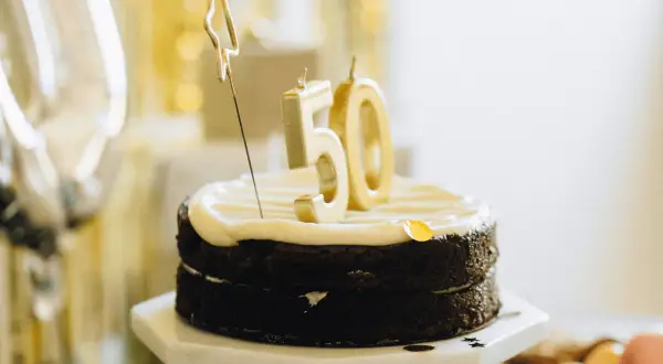 Czekoladowy tort z białym kremem, świeczkami w kształcie cyfry 50 i złotą gwiazdką.