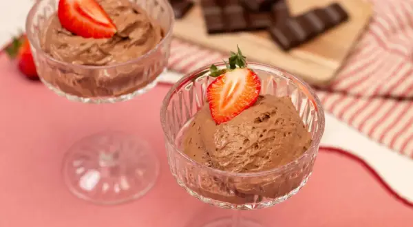 Zwei Gläser mit luftiger Schoko Mousse, garniert mit frischen Erdbeeren. Im Hintergrund liegen Schokoladenstücke.
