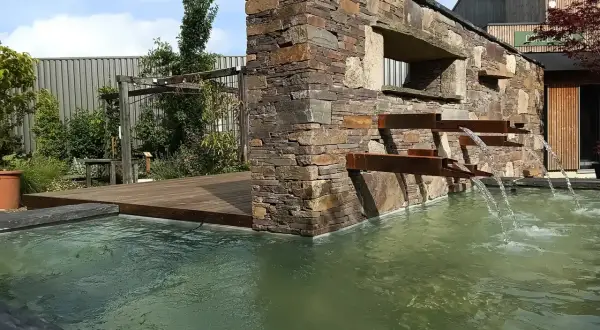 La mare aux plantes, avec sa cascade moderne en pierre et métal, invite à la détente. L'eau ruisselle doucement dans le bassin verdoyant.