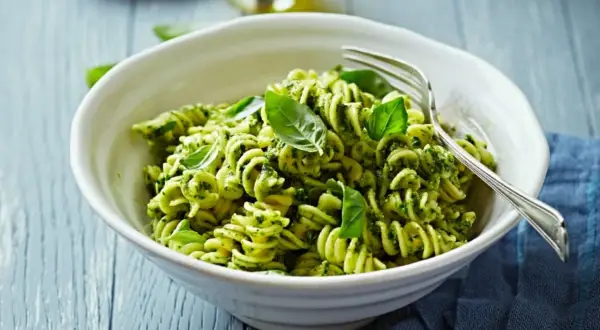 Eine Schüssel Fusilli-Nudeln mit grünem Pesto und frischem Basilikum, garniert mit einer Gabel.