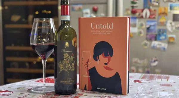 Un bicchiere di vino rosso Nebbiolo d'Alba, una bottiglia e un libro "Untold" sul vino. Le caratteristiche del Nebbiolo sono un viaggio affascinante.