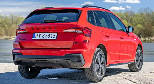 Czerwona Skoda Kamiq z polskimi tablicami rejestracyjnymi, zaparkowana nad wodą. Sprawdź atrakcyjną skoda kamiq cena!