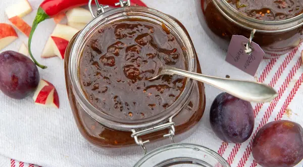 En burk med plommonchutney, perfekt för ett plommon recept. Äpplen, plommon och chili ligger bredvid.