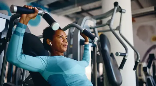 Frau trainiert richtig im Fitnessstudio an einer Brustpresse. Sie konzentriert sich auf die Bewegung und hört Musik über ihre Kopfhörer.