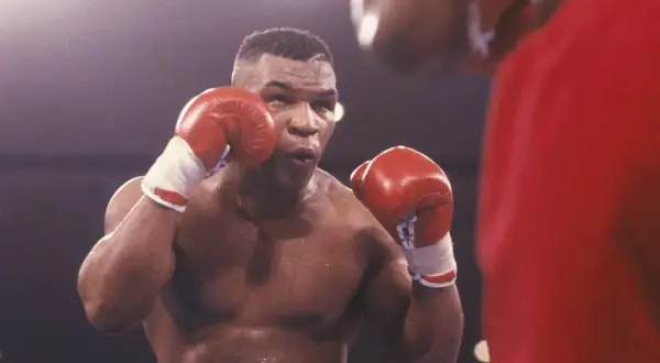 Mike Tyson in his iconic boxing stance, ready to fight. His red gloves are raised, a testament to his legendary career in tysons boxing.