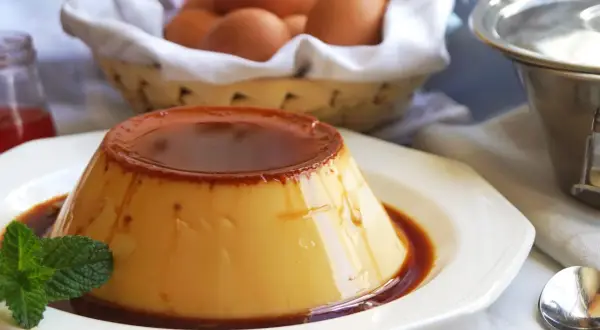 Delicioso flan de huevo de 1 litro, con caramelo líquido y una hoja de menta. En el fondo, huevos frescos en una cesta.