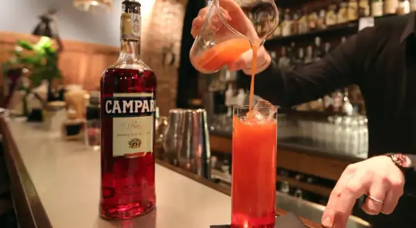Barman nalewa drink z dzbanka do szklanki z lodem. Obok stoi butelka Campari. To właśnie Campari co to za alkohol?