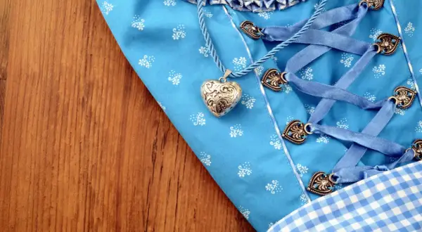 Ein Dirndl-Mieder mit Herzanhänger und Schnürung liegt auf Holz. Bald wird die Dirndlschürze gewaschen.