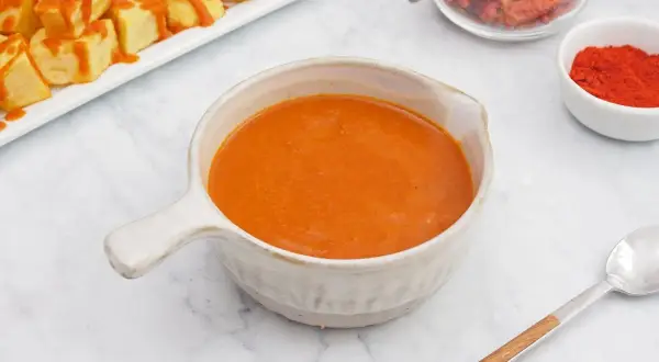 Un cuenco de cremosa salsa brava, lista para acompañar unas patatas. En el fondo, pimentón y guindillas secas.