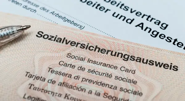 Sozialversicherungsausweis zeigt, wo man die Sozialversicherungsnummer findet. Ein Arbeitsvertrag liegt daneben.