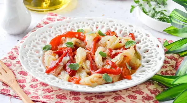 Deliciosa ensalada de bacalao con pimientos rojos asados y hierbas frescas, servida en un plato blanco decorado.
