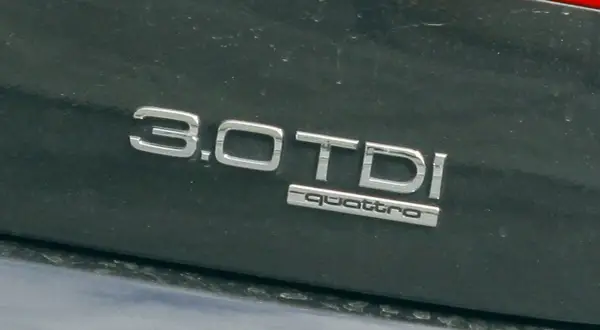 Napis "3.0 TDI quattro" na ciemnym lakierze samochodu. Informuje o pojemności silnika 3.0 litra i napędzie quattro.
