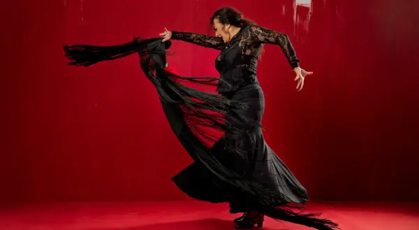 Bailarina de flamenco con mantón negro sobre fondo rojo vibrante.
