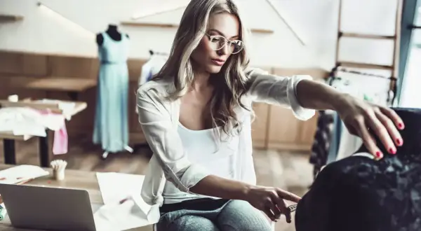 Eine Designerin mit Brille misst Stoff für ihr nächstes Projekt im Bereich IU Modemanagement.