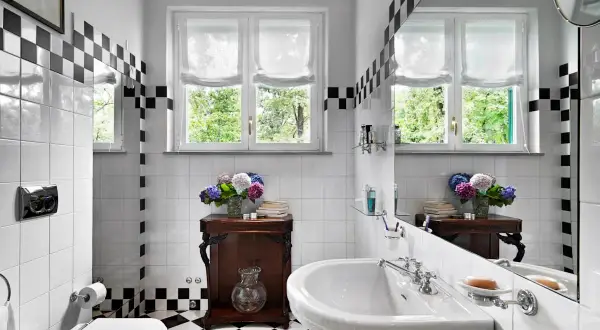 Un elegante bagno bianco e nero vintage con piastrelle a scacchi, un lavabo classico e un vaso di ortensie.