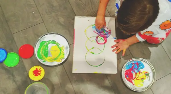 Niño pequeño creando arte con pintura de dedos. Lienzo con círculos de colores y recipientes de pintura.