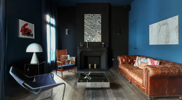 Ein **dunkles Wohnzimmer** mit blau-schwarzen Wänden, Ledersofa, Kamin und moderner Kunst.