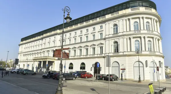 Elegancki, biały budynek hotelowy z kolumnami i łukowymi oknami, przed którym zaparkowane są samochody.