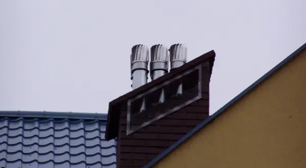 Trzy obrotowe nasady kominowe wentylacyjne na ceglanym kominie, chroniące przed wiatrem i deszczem.