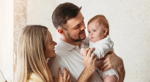 Uśmiechnięta mama i tata patrzą na swoje dziecko, które właśnie zaczyna rozpoznawać twarze.