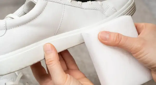 Manos limpiando zapatillas blancas piel con una esponja mágica. ¡Devolviendo el brillo a tus zapatos!