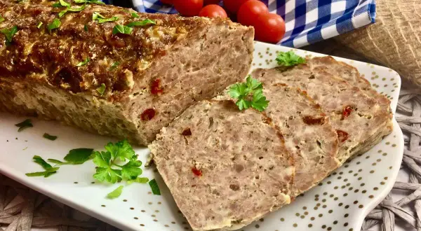 Pyszna pieczeń z jajkiem, pokrojona w plastry, ozdobiona natką pietruszki. Obok wiązka pomidorków koktajlowych.