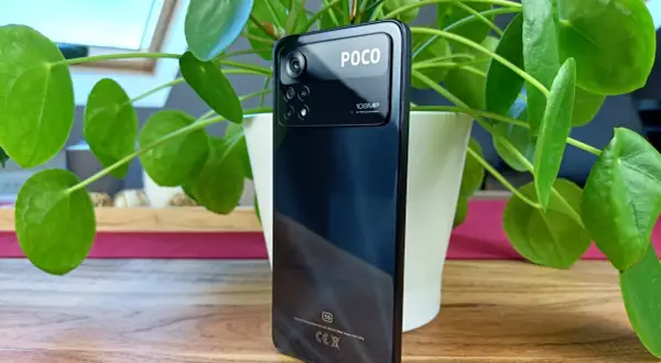Czarny smartfon POCO X4 z potrójnym aparatem 108MP, otoczony zielonymi liśćmi rośliny.