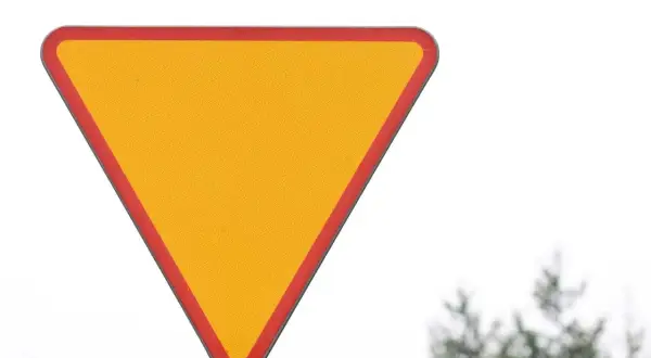 Żółty trójkąt z czerwoną obwódką, znak ustąp pierwszeństwa, ostrzega przed zbliżającym się skrzyżowaniem.