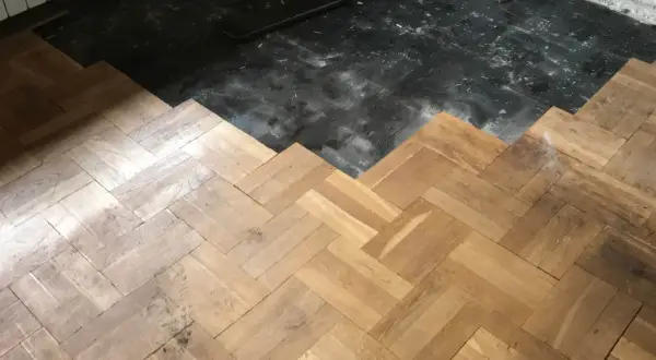 Drewniana podłoga w jodełkę częściowo odsłania czarną, starą warstwę. Rozważasz usuwanie subitu? Cena tej usługi zależy od wielu czynników.