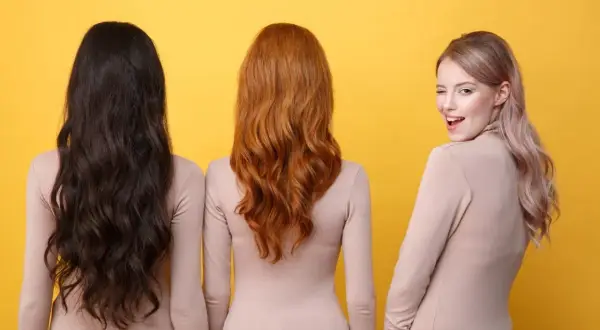 Trzy kobiety prezentują modne kolory włosów: kruczoczarne, rudoczerwone i pastelowy blond. Jedna z nich mruga do widza.