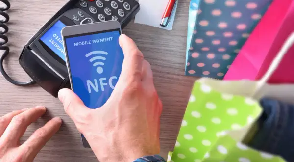 Płatność zbliżeniowa telefonem z funkcją NFC. Transakcja w toku, obok kolorowe torby na zakupy.