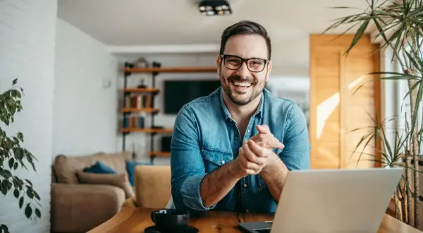 Hombre sonriente con portátil, buscando ideas para negocios rentables en un pueblo.