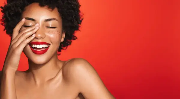 Une femme rit, la main sur le visage, avec un rouge à lèvres éclatant. Quelle couleur de rouge à lèvres !