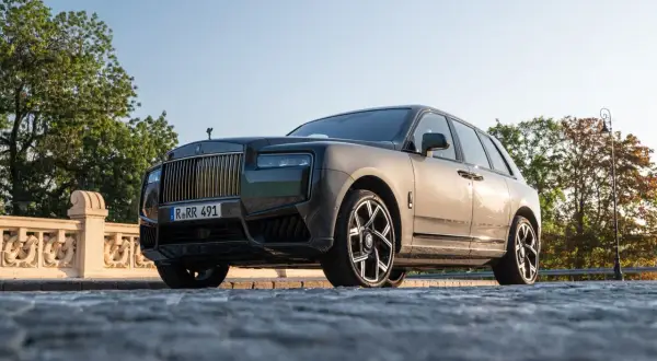 Elegancki Rolls-Royce Cullinan na kamienistej drodze, z grillem i charakterystyczną figurką na masce.