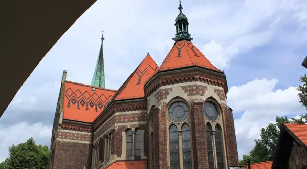 Suchanino kościół z zieloną wieżą i ceglaną fasadą, ozdobiony czerwonymi dachami i ozdobnymi oknami.