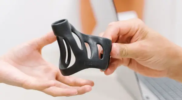 Zwei Hände halten ein schwarzes, 3D-gedrucktes Objekt. Ein schnellender Finger zeigt auf die feinen Details.